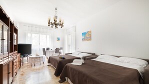 Ein Hotelzimmer mit zwei Betten, einem Fernseher, einer Chandelüster, einem Esstisch und einem Gemälde an der Wand.
