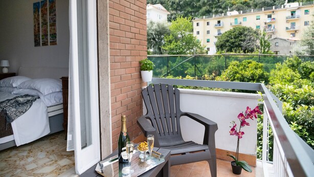 Ein Balkon mit einem Bett, einem Stuhl, einem Tisch mit einer Flasche und Gläsern sowie einer Topforchidee.
