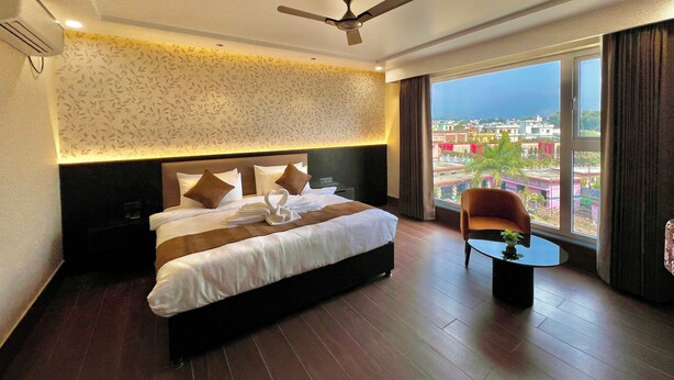 A hotel room with a large bed, a ceiling fan, a view of the city, and a small table with a plant.