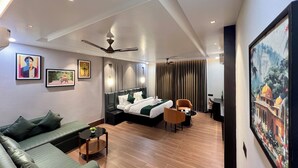 A modern hotel room with a bed, sofa, and a dining area.