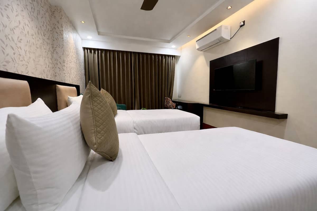 Habitación de hotel con dos camas, un televisor de pantalla plana montado en la pared y un equipo de aire acondicionado.