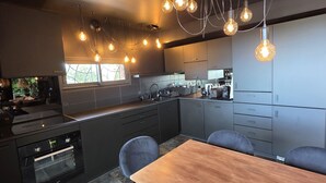 Een moderne keuken met een ingebouwde oven, een eettafel met stoelen en hanglampen.