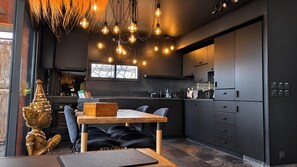 A modern kitchen with dark cabinetry, a wooden dining table, and pendant lighting. - Villa Lâo: 220m² with a swimming pool, sauna and panoramic views of Lake Salagou (Le Bosc)