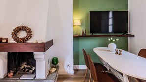 En matplats med en öppen spis, en tv som är monterad på väggen och ett bord med stolar.