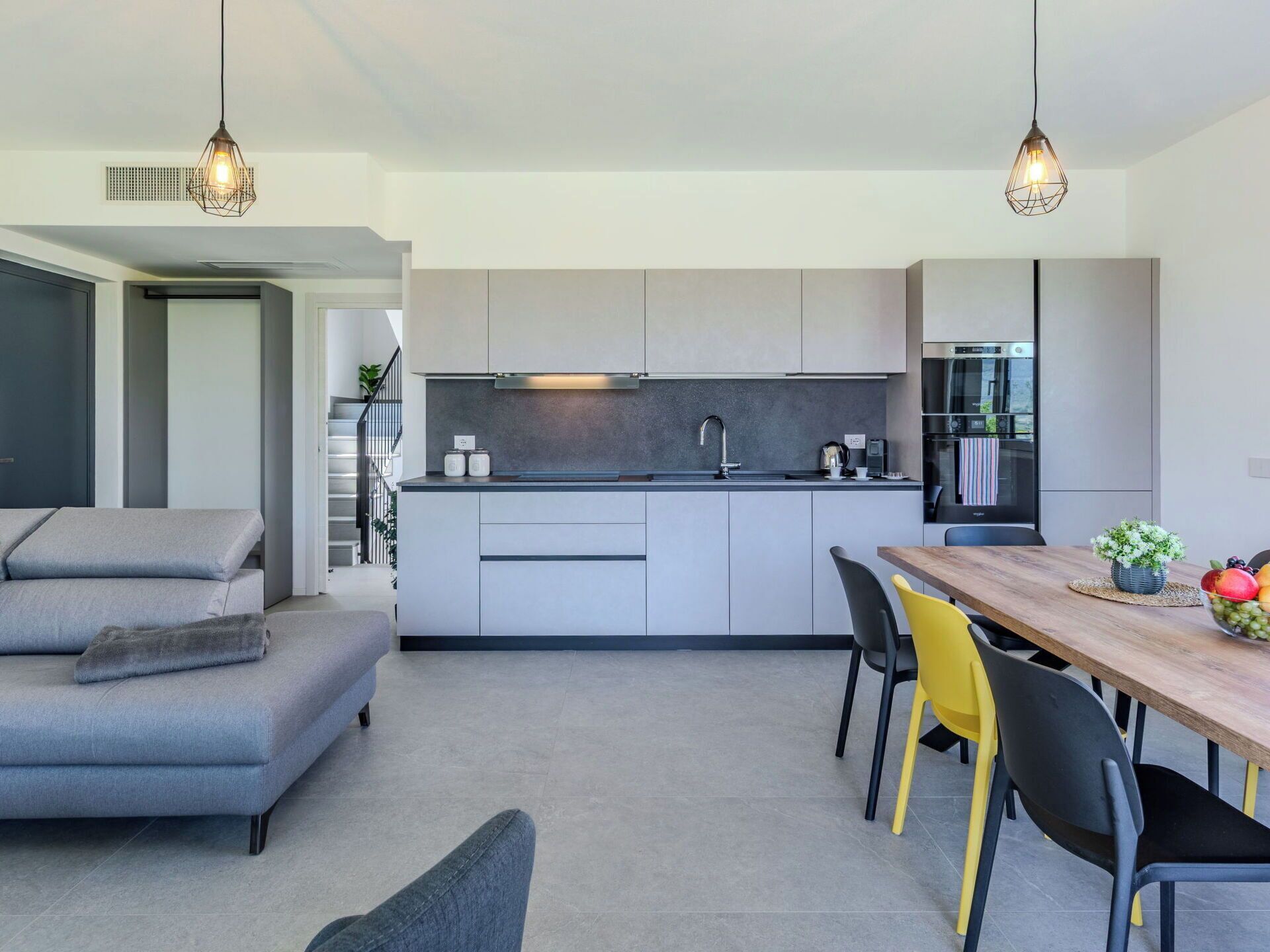A modern kitchen with a central island, grey cabinetry, and a dining area with a wooden table and chairs.