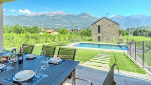 Ein Essbereich mit Tisch für vier Personen, einem Pool und einem Gebäude aus Stein im Hintergrund.