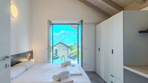 Ein modernes Schlafzimmer mit einem großen Bett, einem Kleiderschrank und einem Balkon mit Blick auf die Berge.