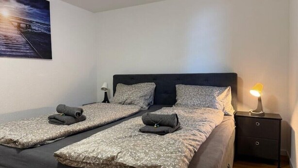 A double bed with a headboard, two bedside tables, and a nightstand with a lamp. - Happy Life 2-20min Interlaken-Panoramic view of mountains (Wimmis)
