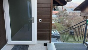A wooden exterior with a glass door, a metal staircase, and a view of a mountainous landscape. - Happy Life 2-20min Interlaken-Panoramic view of mountains (Wimmis)