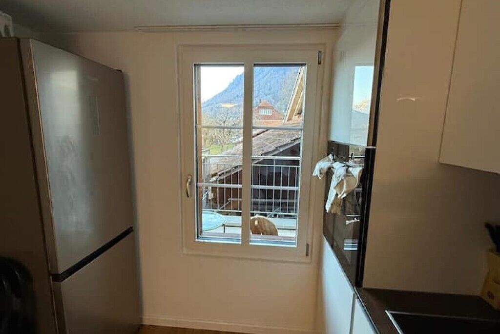 Eine kleine Küche mit Fenster, Kühlschrank und Schränken.