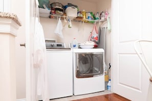 A laundry room with a washing machine, dryer, and shelves with cleaning supplies. - Waterfront Resort | Community Amenities | Sleeps 13 (Selbyville)