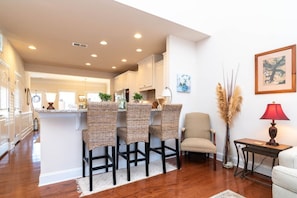 A modern kitchen with bar stools, a dining area with a chair, and a small table with a lamp. - Waterfront Resort | Community Amenities | Sleeps 13 (Selbyville)