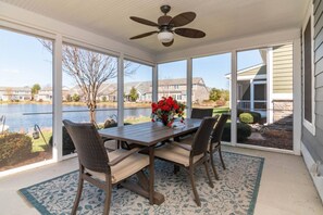 A covered patio with a table and chairs, a ceiling fan, and a view of a lake and houses. - Waterfront Resort | Community Amenities | Sleeps 13 (Selbyville)