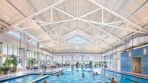 An indoor swimming pool with multiple lanes, a high ceiling with a geometric design, and large windows allowing natural light. - Waterfront Resort | Community Amenities | Sleeps 13 (Selbyville)