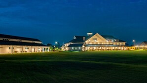 A large building with multiple sections, a covered outdoor area, and a well-lit lawn at dusk. - Waterfront Resort | Community Amenities | Sleeps 13 (Selbyville)