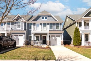 A multi-story residential building with a front porch, garage, and a vehicle parked in front. - Waterfront Resort | Community Amenities | Sleeps 13 (Selbyville)