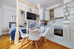 A modern kitchen with white cabinets, a built-in oven, and a dining area with a round table and white chairs. - Charming studio apartment with a view of the sea in Novi Vinodolski (Novi Vinodolski)