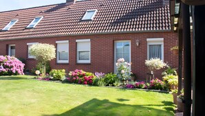 Een gebouw van rode bakstenen met een pannendak, meerdere ramen en een verzorgde tuin met diverse bloemen en struiken.