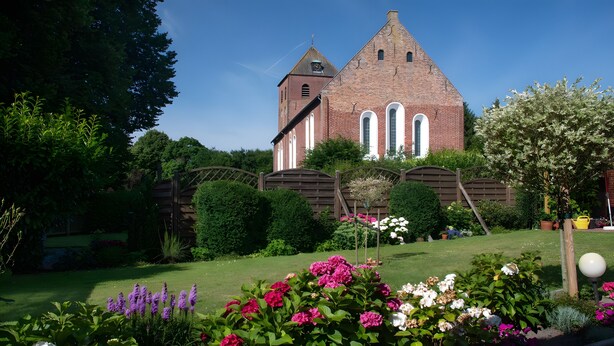 Een kerk met een opvallende toren en boogvensters, omringd door een verzorgde tuin met verschillende bloemen en struiken.