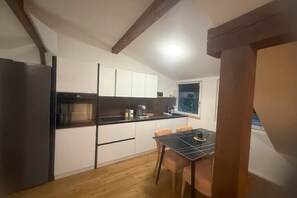 A compact kitchen with a refrigerator, oven, and a dining table with chairs. - Happy Life 3-20 min. Interlaken 5 min. Spiez/Thun (Wimmis)