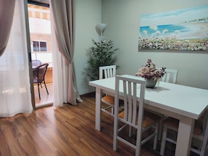 A dining area with a white table and chairs, a potted plant, and a painting of a beach scene on the wall. - Torrevieja 2 BR and Parking (Torrevieja)