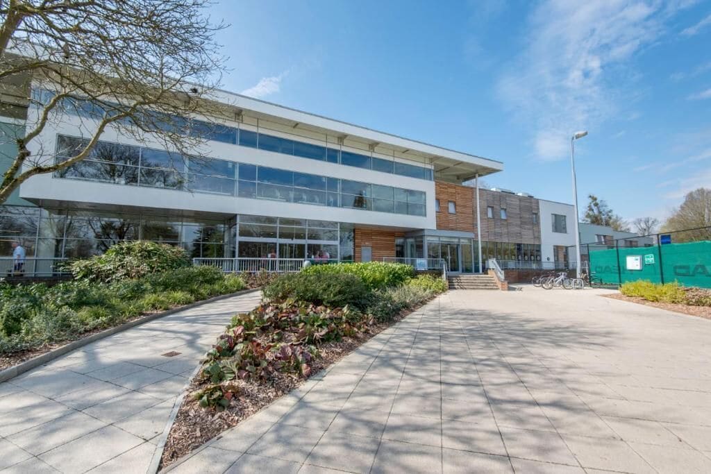A modern building with large windows, a covered walkway, and a landscaped area with plants.