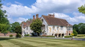 A large stone building with multiple chimneys, arched windows, and a well-maintained lawn. - Bisham Abbey National Sports Centre  (Bisham)