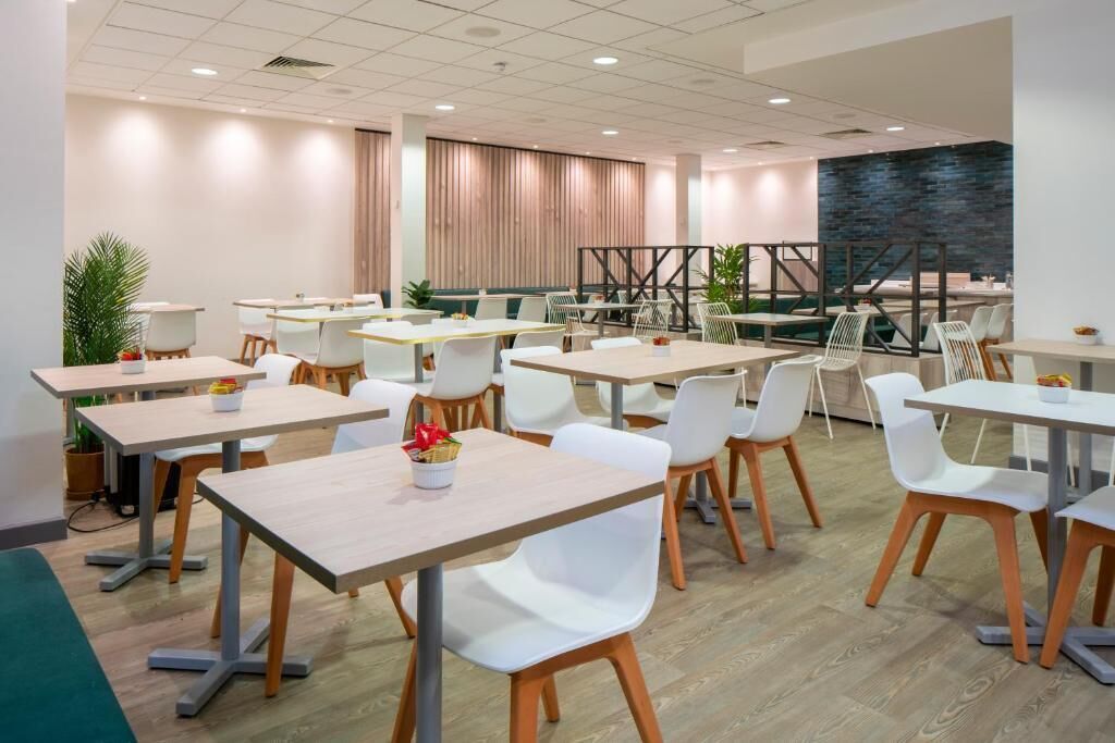 A modern dining area with multiple tables and chairs, a wooden floor, and a large stone wall.