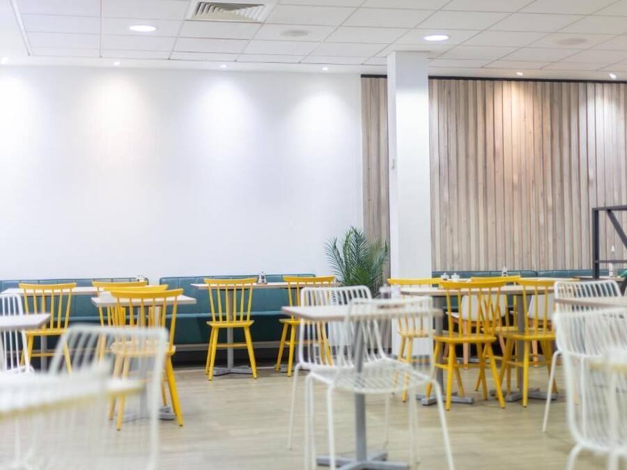 A conference room with tables and chairs, a green sofa, and a wooden panel wall.