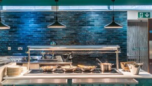 A buffet setup with multiple serving stations, a tiled backsplash, pendant lighting, and a visible exit sign. - Bisham Abbey National Sports Centre  (Bisham)