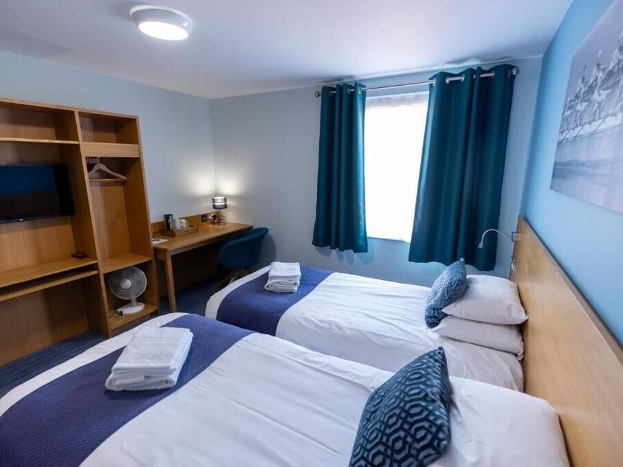 A hotel room with two beds, a desk, a TV, and a wardrobe.
