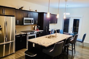 A modern kitchen with dark cabinets, stainless steel appliances, a granite countertop, and pendant lighting. - Harbour Landing Family Home (Regina)
