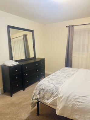 A bedroom with a bed, a dresser, a mirror, and a window with curtains.