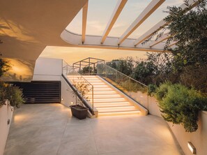Un escalier moderne avec des rampes en verre, entouré de verdure et menant à un niveau supérieur.