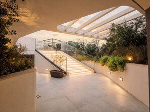 Un intérieur moderne avec un escalier en verre, un plafond plat et une vue sur la verdure environnante.
