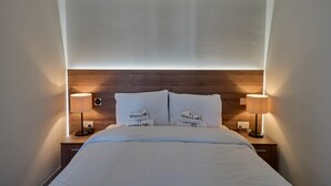 Een net opgemaakt bed met witte lakens, twee bedlampen en een houten hoofdbord.