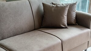 En moderne stue med en beige sofa, to puder, et glasbord og udsigt ud