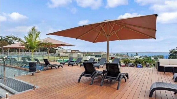 A rooftop deck with lounge chairs, a pool, and a view of the ocean. - Coastal Breeze Nelson Bay: King Bed, Spa bath, Private balcony, Resort pool (Nelson Bay)