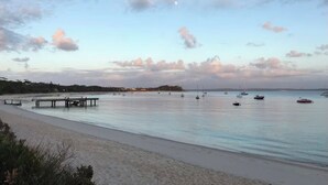 A beach with a pier extending into calm waters, boats, and a clear sky. - Coastal Breeze Nelson Bay: King Bed, Spa bath, Private balcony, Resort pool (Nelson Bay)