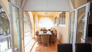Uma área de refeições com mesa e cadeiras, um ventilador de teto e janelas amplas.