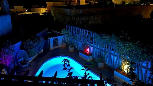 Vista noturna de uma área de piscina no terraço, com piscina, plantas em vasos e uma grade.