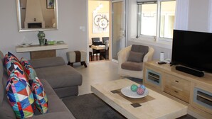 Uma sala de estar com sofá, poltrona, mesa de centro, televisão e um espaço de jantar com cadeiras e mesa.