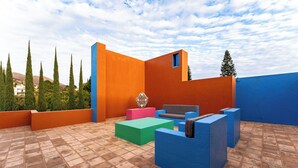 Eine Dachterrasse mit Fliesenboden, einer blauen und orangefarbenen Wand sowie einer Sitzecke mit Tisch und Stühlen.