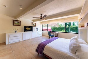 A bedroom with a bed, a desk, a chair, a television, and a window with a view of greenery.