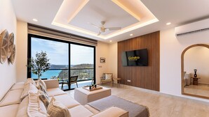 Un salon moderne comprenant un canapé, une table basse, un téléviseur et une grande fenêtre donnant sur la mer.