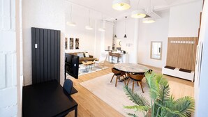 Ein modernes Wohnzimmer mit Fernseher, Sofa, Esstisch und Pflanzen.