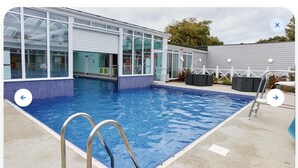 En swimmingpool med et glashus, en metalstige og et afspærret område med udendørs siddepladser.