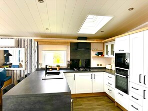 Una cocina moderna con armarios blancos, una isla central, horno empotrado y un ventanal grande.