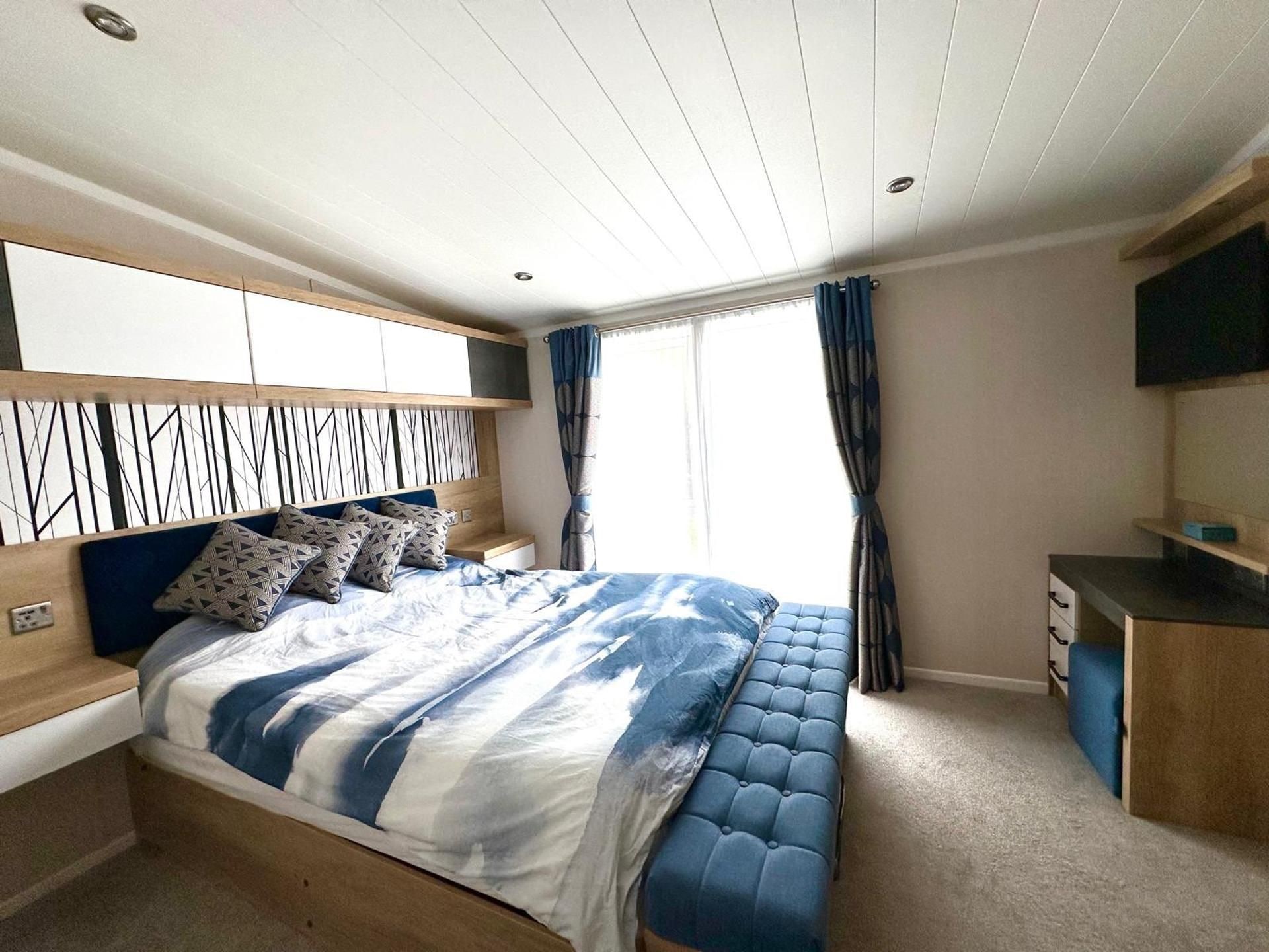 A bedroom with a bed, bedside tables, a desk, and a TV.