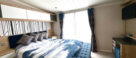 A bedroom with a bed, bedside tables, a desk, and a TV.